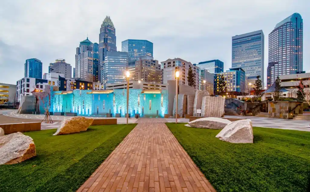 Charlotte, North Carolina skyline with a central grass and brick walkway leading to Romare-Bearden Park, framed by the backdrop of the city skyline.
